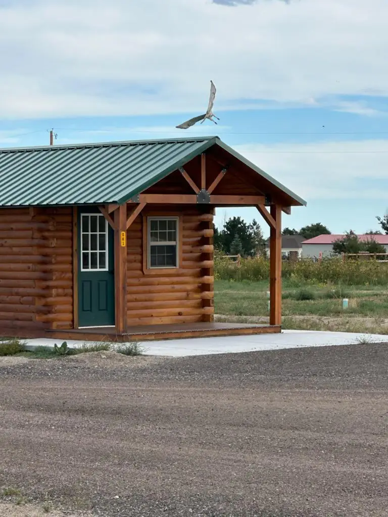 Green-roofed log camping cabin with covered porch on a sunny day